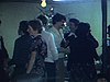 Famille réunie au sous-sol, un couple danse, les autres assis autour de la table de billard, on parle et on s’embrasse, un couple s’embrasse et la femme tombe