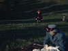 Famille en très beaux habits fait un pique-nique sur une couverture, une femme tient un bébé dans ses bras et lui donne le biberon, les enfants courent en tenant la main de leur père, gros plans des enfants qui sourient
