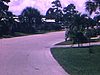 Plusieurs maisons mobiles en Floride, une femme en maillot de bain pose pour la caméra, des hommes déchargent l’auto, un homme filme le caméraman avec sa caméra 