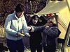 Une femme et deux filles se brossent les cheveux près d’une tente dans un champ - 1976