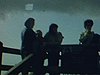 une femme marche sur un chemin de pierre, des gens regardent au loin sur un pont, une femme pose sur uns structure de métal