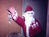 Père Noel avec une barbe en ouate arrive au salon, les enfants font la file pour recevoir leurs cadeaux, ils les déballent en vitesse, deux enfants posent sur les genoux du père Noel en saluant la caméra
