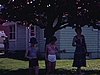 Une femme et deux filles sous un arbre avec des fleurs roses, l'une des filles joue au yoyo