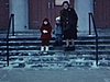 Une femme et deux enfants sortent de l’église, ils ont leurs beaux manteaux, descendent les marches et vont vers la caméra 1963