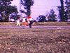Partie de baseball sur un terrain dans un champ, gros plan sur une fille qui sourit à la caméra (1971-72)